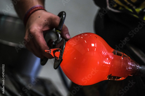 Artist glass blower working glass paste on his workbench. A glass crafter is burning and blowing an art piece photo