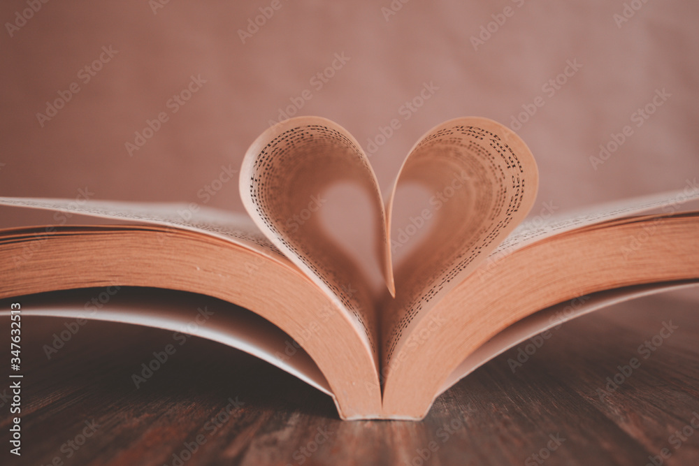 Soft background of an open book with heart shape from paper pages on wooden table close up Soft background of an open book with heart shape from paper pages on wooden table close up