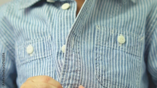 Montessori practical life skills & Early child milestones development concept. Close up of cute Asian child unbutton blue shirt in slow motion. Learn to get dressed on his own with confidence.