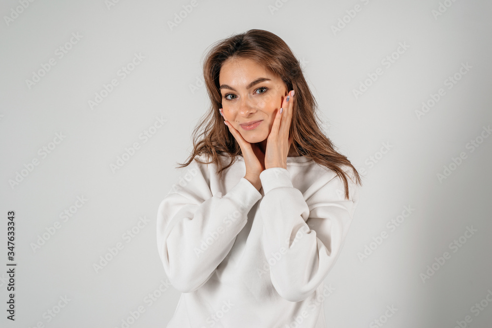 Young beautiful woman standing on the white background holding her hands near tha face Young beautiful woman standing on the white background holding her hands near tha face