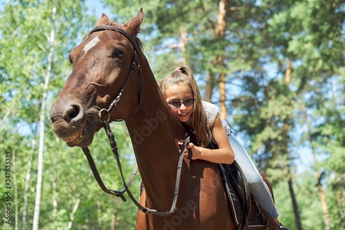 Girl child riding horse, summer horse ride in the forest, girl lovingly hugged horse © Valerii Honcharuk