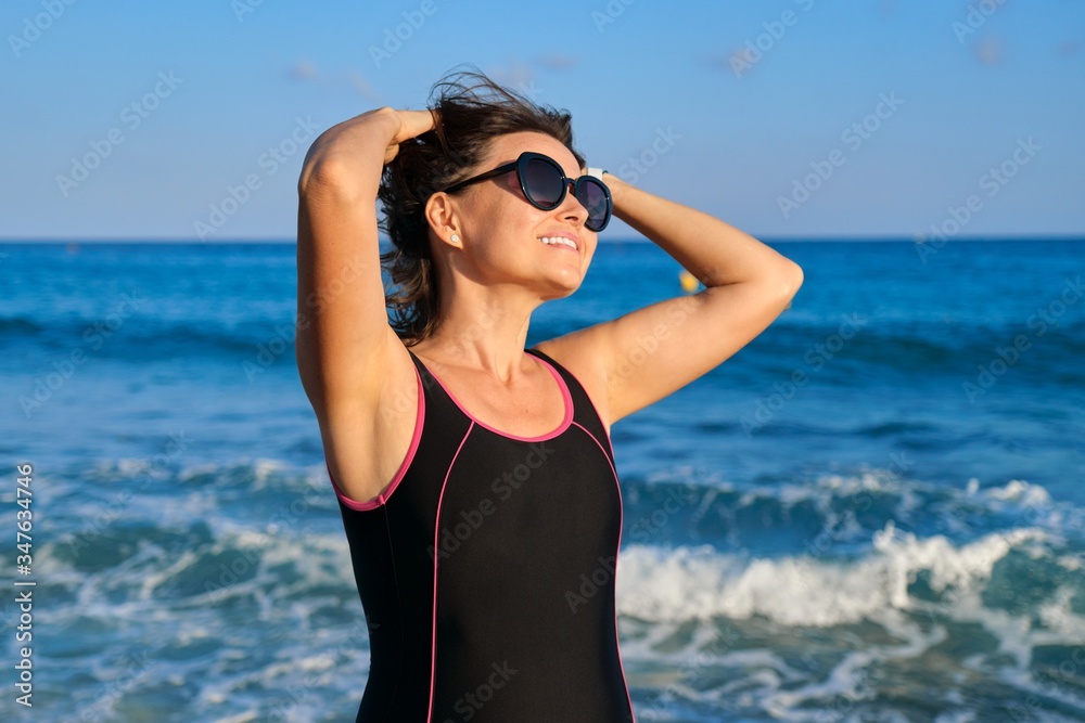 Portrait of mature woman in sunglasses swimsuit enjoying sea sunset