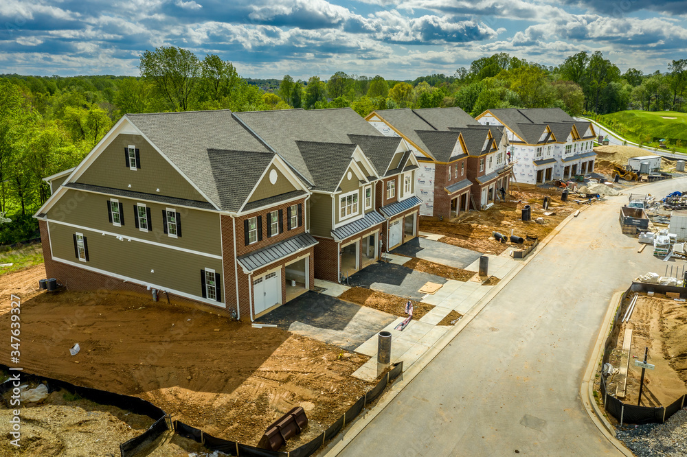 Elevated view of almost finished luxury townhouses with two single car garages, brick and shake and shingle siding, gable roof with attic vent on a new residential development in Maryland USA