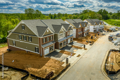 Elevated view of almost finished luxury townhouses with two single car garages, brick and shake and shingle siding, gable roof with attic vent on a new residential development in Maryland USA