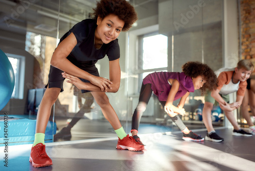 Join a healthier way. Portrait of a boy smiling at camera while warming up  exercising together with other kids in gym. Sport  healthy lifestyle  active childhood concept