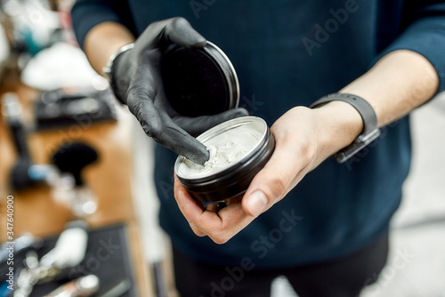 Hair cosmetic. Cropped photo of a barber using wax or gel for hair styling while working in barbershop or salon photo