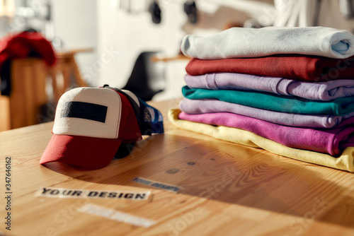 Labels that enhance your image. Custom apparel, clothes neatly folded on shelves. Stack of colorful clothing and baseball cap in the store