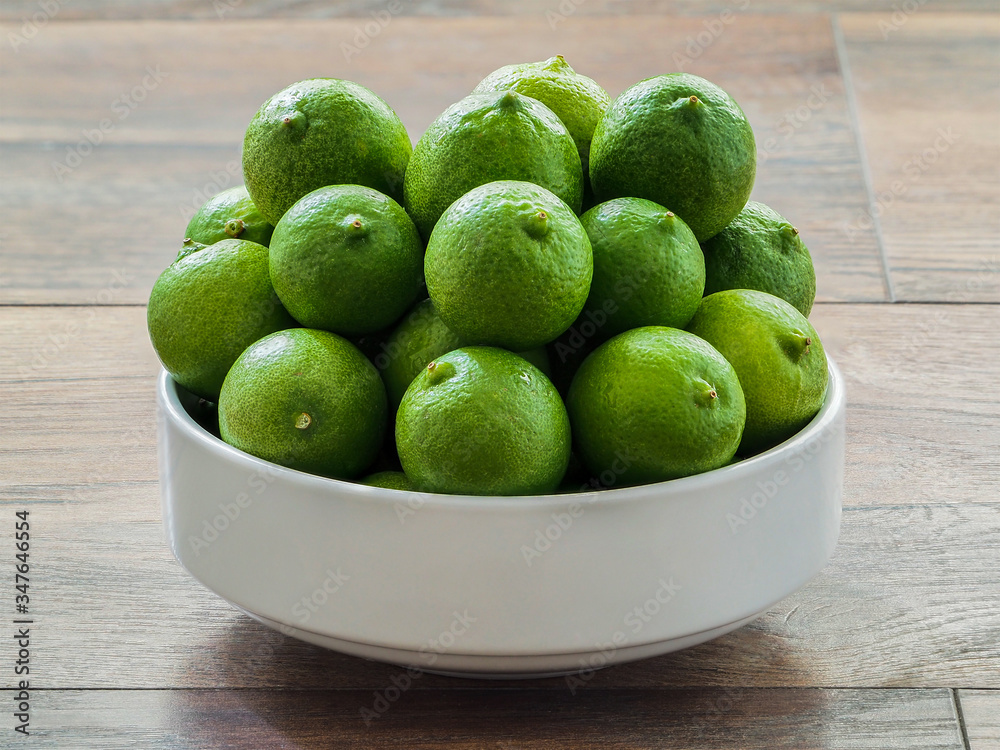 Green lemons in a white bowl on wood Green lemons in a white bowl on wood