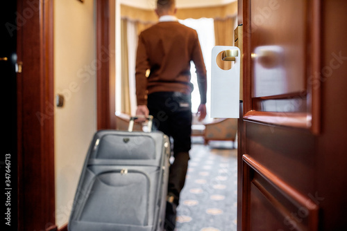 Another Home. Cropped shot of middle-aged businessman in casual wear with suitcase entering his room in the background. A door with a sign at the front. © Svitlana
