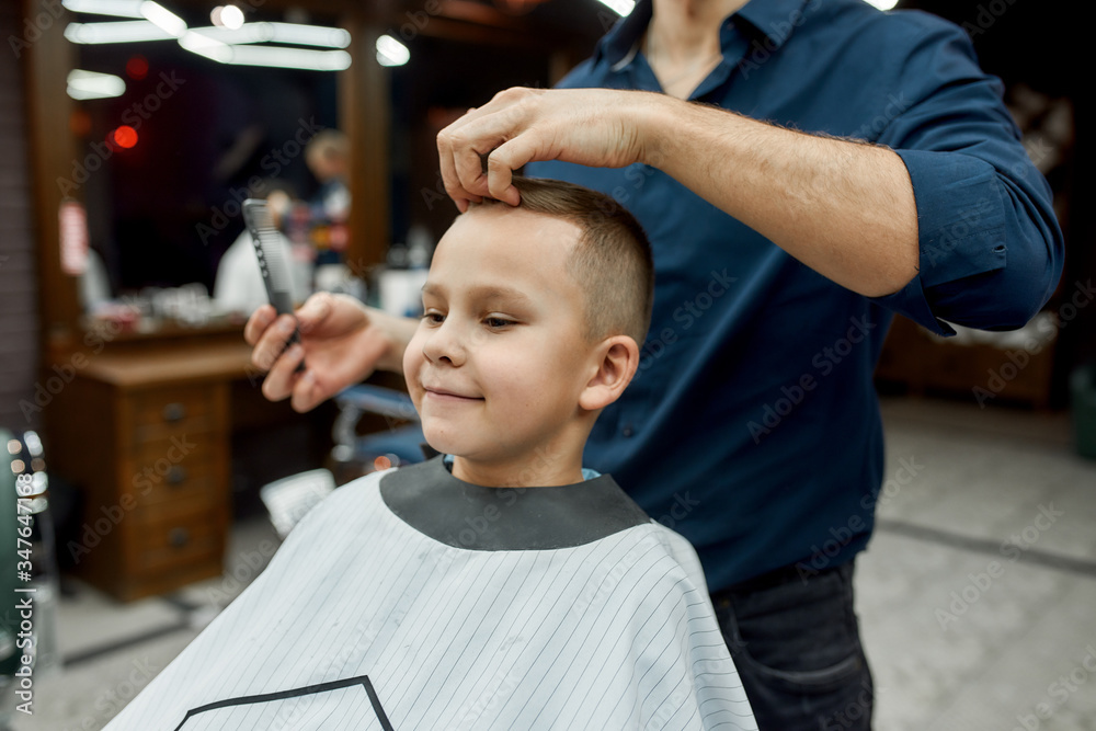Little man. Cute boy sitting in a barbershop chair and smiling while male barber styling his hair. Barbershop Little man. Cute boy sitting in a barbershop chair and smiling while male barber styling his hair. Barbershop