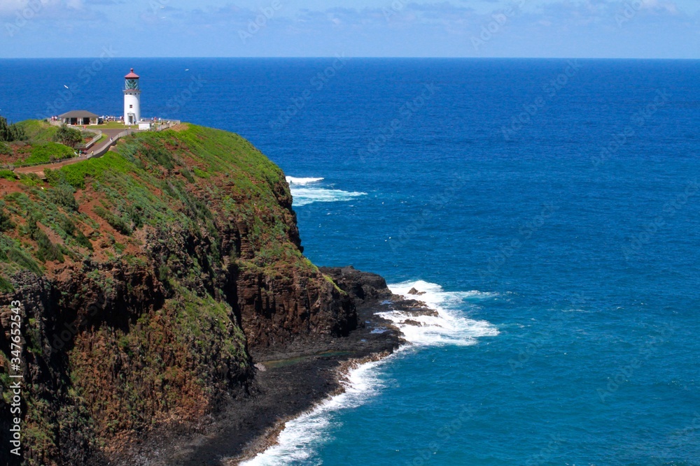 White Lighthouse set atop a cliff with a brilliant blue ocean in the background in Kauai, Hawaii, USA.