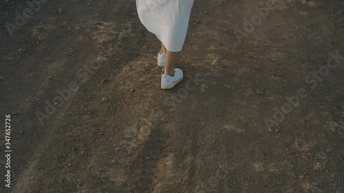 A girl walks along the summer island during sunset. Legs of a girl in beauties and a long white dress walk on mountains, stones. Atmospheric video photo