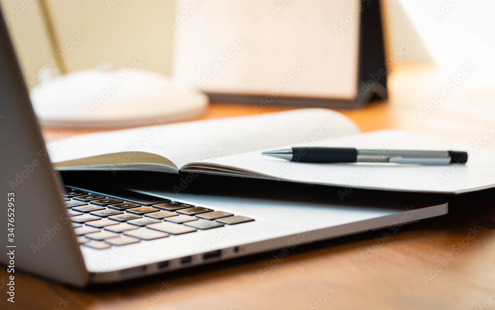Laptop Computer on a Modern Wooden Business Desk with a Notepad and Pen in Unfocused Background.