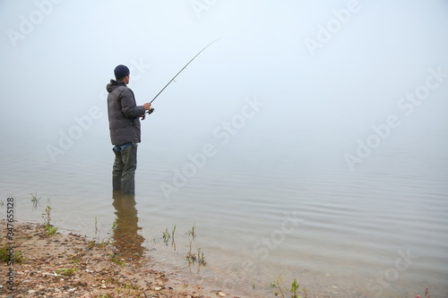 fisherman holding fishing rod on the lake in fog
