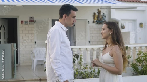 a couple is talking near his villa on vacation or at home in white clothes, the guy is yelling at the girl, but the girl laughs off and everything is fine. Humor in a relationship, quarrel photo