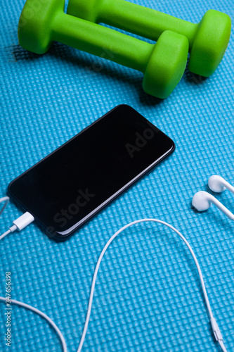 two green dummbells with smartphone with blank screen and headphones on blue exercise mat photo