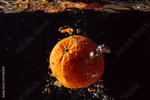 orange falling into the water against a black background and air bubbles rising upwards
