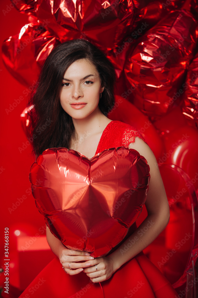 Woman with Hearts Balloons on a red background. Beauty Girl on Valentine's Day. Model in a stylish red dress. Woman with Hearts Balloons on a red background. Beauty Girl on Valentine's Day. Model in a stylish red dress.