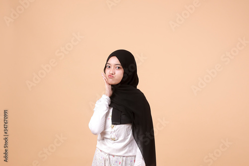 Portrait of happy young Muslim Asian Girl laughing hard with big open mouth, over orange background. Indonesian woman © Mohammad