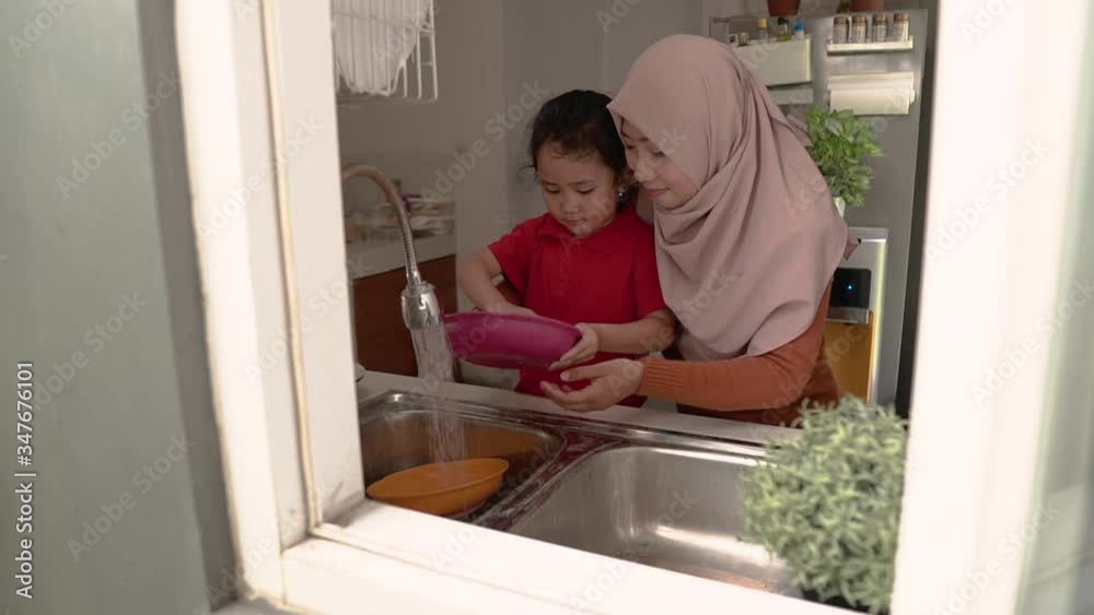Helping hand. Cute little Girl Help Her muslim Mother In Washing Dishes At Family Kitchen Helping hand. Cute little Girl Help Her muslim Mother In Washing Dishes At Family Kitchen
