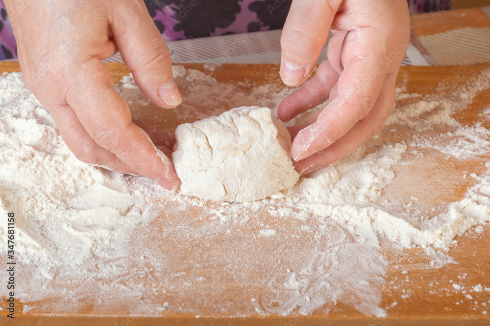 Female hands sculpt a bunch of raw dough on a wooden board with flour. Close-up Female hands sculpt a bunch of raw dough on a wooden board with flour. Close-up