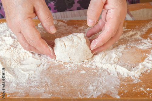 Female hands sculpt a bunch of raw dough on a wooden board with flour. Close-up