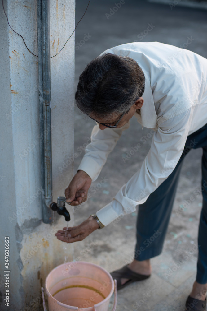 portrait of an Indian old man washing his hands in a tap water on a rooftop during sunset in home isolation.Indian lifestyle, disease and home quarantine. portrait of an Indian old man washing his hands in a tap water on a rooftop during sunset in home isolation.Indian lifestyle, disease and home quarantine.
