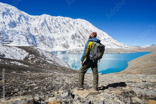 Travel and hikking concept: Trekker with backpack on Tilicho lake. Its 4900m above sea level. Snowly peaks of mountains and Tilicho lake on background. photo