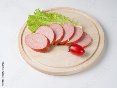 Raw smoked sausage, cut into slices on a board. Near leaf lettuce and tomato