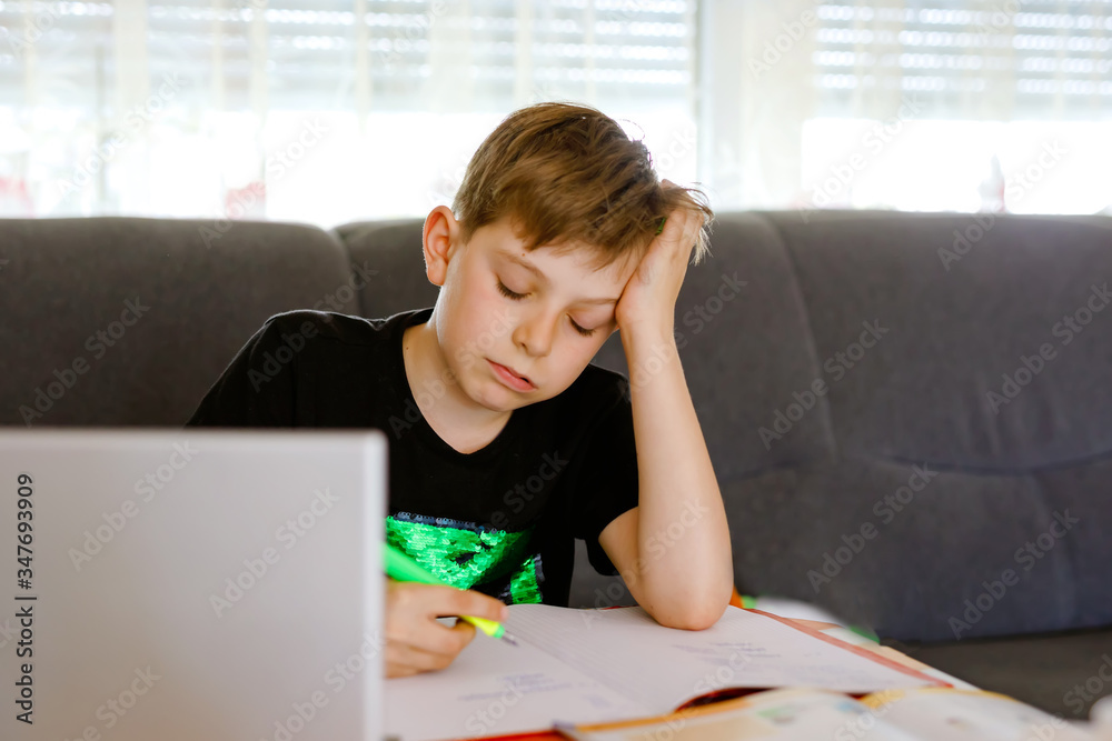 Upset school kid boy making homework during quarantine time from corona pandemic disease. Frustrated sad boy learning staying at home with video via laptop. Homeschooling concept Upset school kid boy making homework during quarantine time from corona pandemic disease. Frustrated sad boy learning staying at home with video via laptop. Homeschooling concept