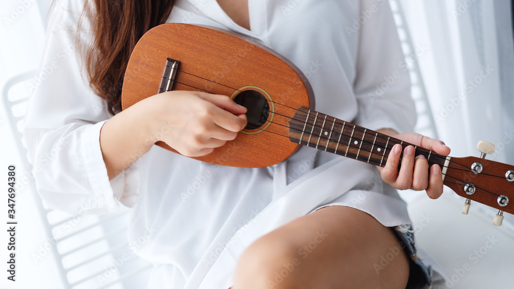 Fototapeta premium Closeup image of a woman sitting and playing ukulele in bedroom
