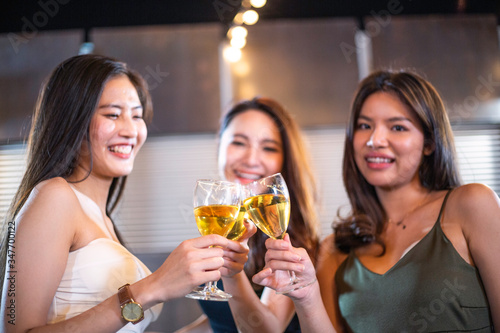 Group of happy smiling Asian girl friends celebrating party with champagne toasting drinks at rooftop cafe together  female gang chatting  laughing  night lifestyle of young people  focus on glasses