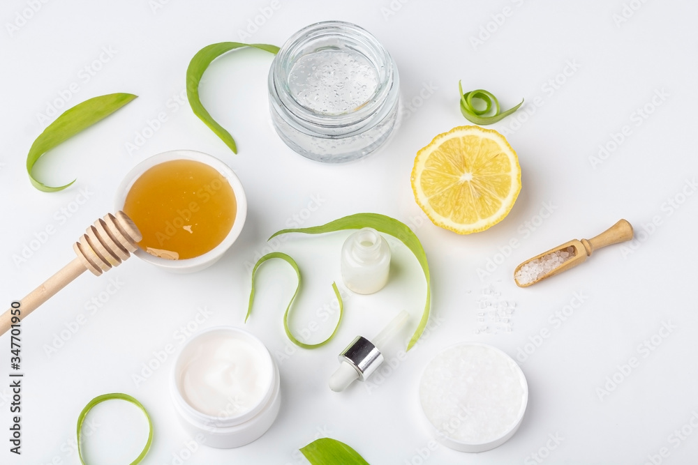 Natural organic ingredients to make home skin care. Cleansing and nourishing cosmetics. Beauty products: cream, honey, sea salt among green leaves on white background. Close up, copy space for text Natural organic ingredients to make home skin care. Cleansing and nourishing cosmetics. Beauty products: cream, honey, sea salt among green leaves on white background. Close up, copy space for text