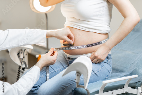 Doctor measuring pregnant woman's belly with a tape during a medical examination, cropped view without face focused on the abdomen