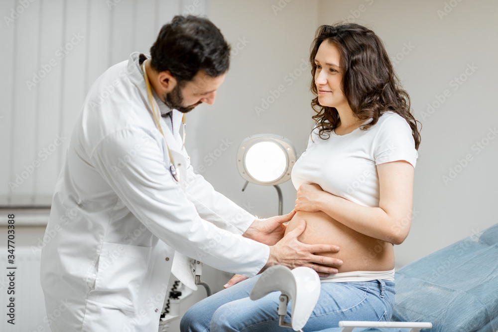Fototapeta premium Male doctor makes a massage of the abdomen of pregnant woman during a medical examination in the office. Concept of medical care and health during a pregnancy