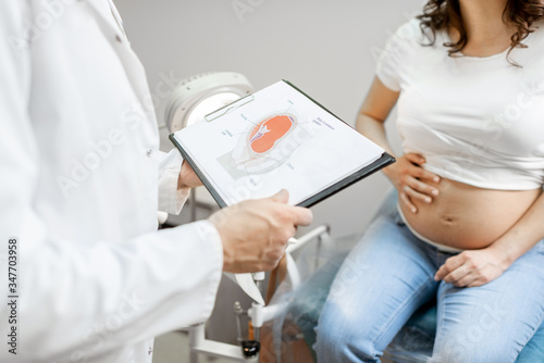 Doctor with pregnant woman during a medical consultation in gynecological office  showing some medical schemes for understanding  cropped view without faces