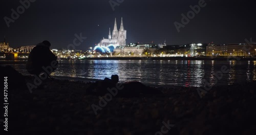 Smooth Slide of Cologne Cathedral and Hohenzollernbridge in the background and a observing person, rhine river with rocks in the foreground. photo