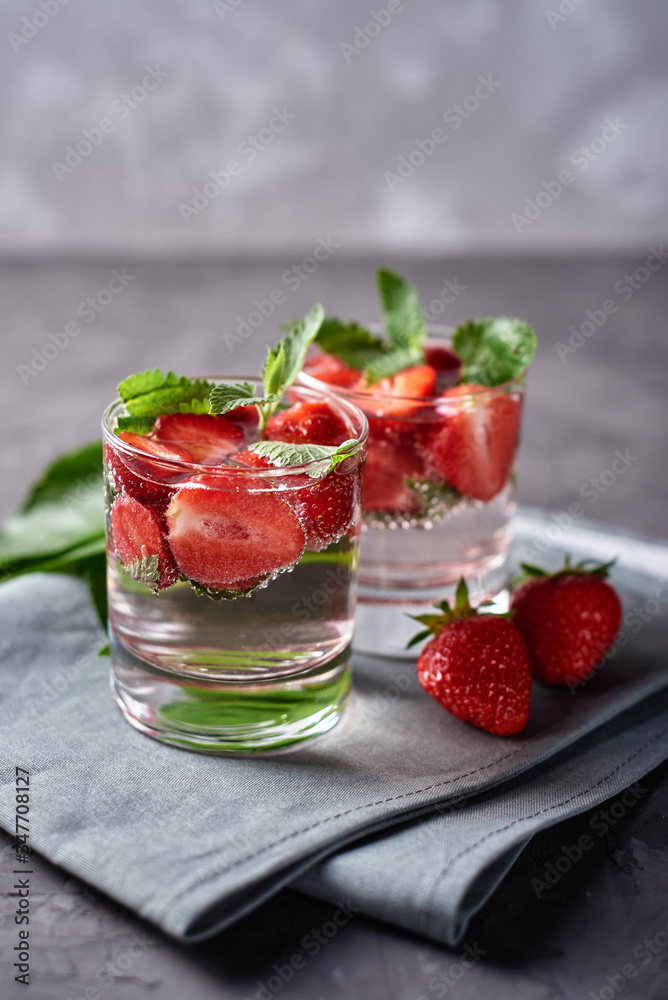 Water with strawberry and mint in sparkling glasses on gray napkin on concrete table, copy space. Cold summer drink. Mineral water Water with strawberry and mint in sparkling glasses on gray napkin on concrete table, copy space. Cold summer drink. Mineral water