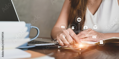 Cropped of woman sitting in front her computer laptop and coffee while using/touching a smartphone with showing virtual icons graphic/interface on screen. User interface icon concept.