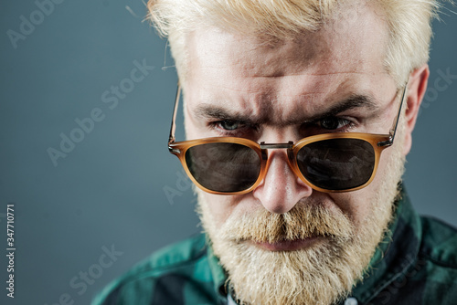 Bearded man with fashion sunglasses. Close-up portrait of cheerful young man on gray background with copy space.