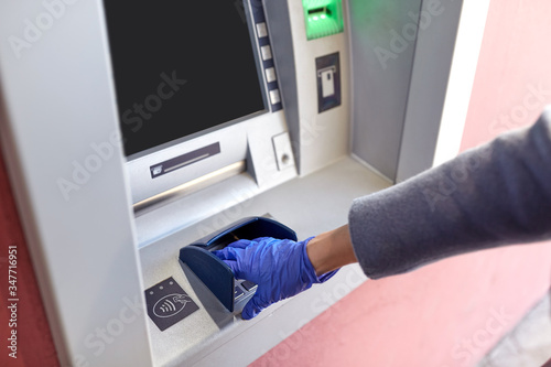 finance, bank and hygiene concept - close up of hand in medical glove entreing code at atm machine