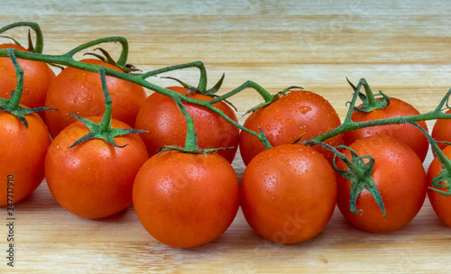 Fresh cherry tomatoes on branch on bamboo wooden table background. Cherry tomatoes on cutting board