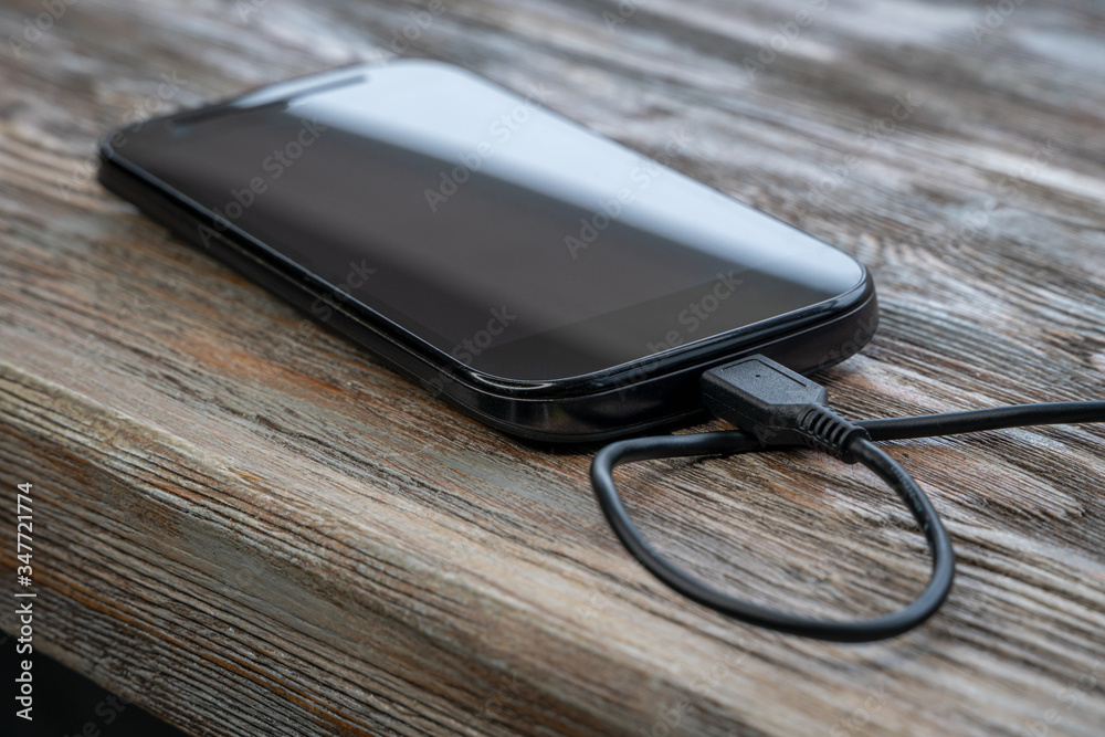 Smartphone charging with power bank on wooden table. Phone Connected to charger Smartphone charging with power bank on wooden table. Phone Connected to charger