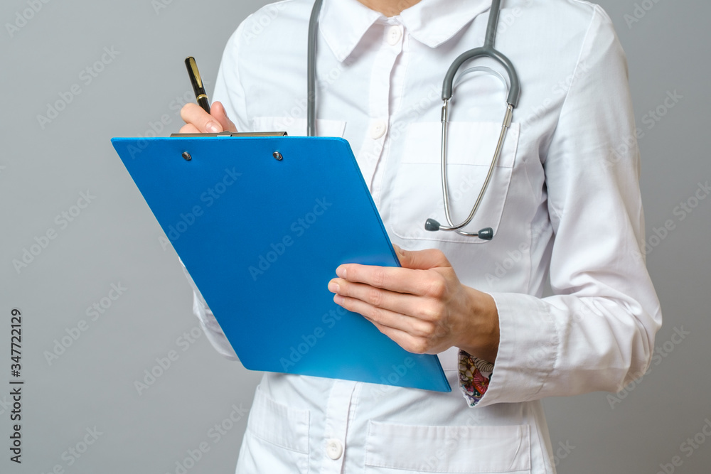 Young woman physician with stethoscope prescribing treatment to patient. Female doctor with pen writing recipe on clipboard. Isolated on gray