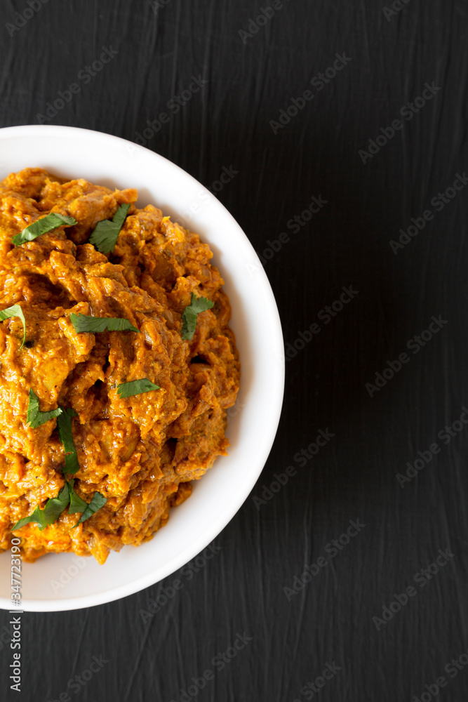 Homemade Chicken Tikka Masala in a white bowl on a black surface, top view. Flat lay, overhead, from above. Copy space. Homemade Chicken Tikka Masala in a white bowl on a black surface, top view. Flat lay, overhead, from above. Copy space.
