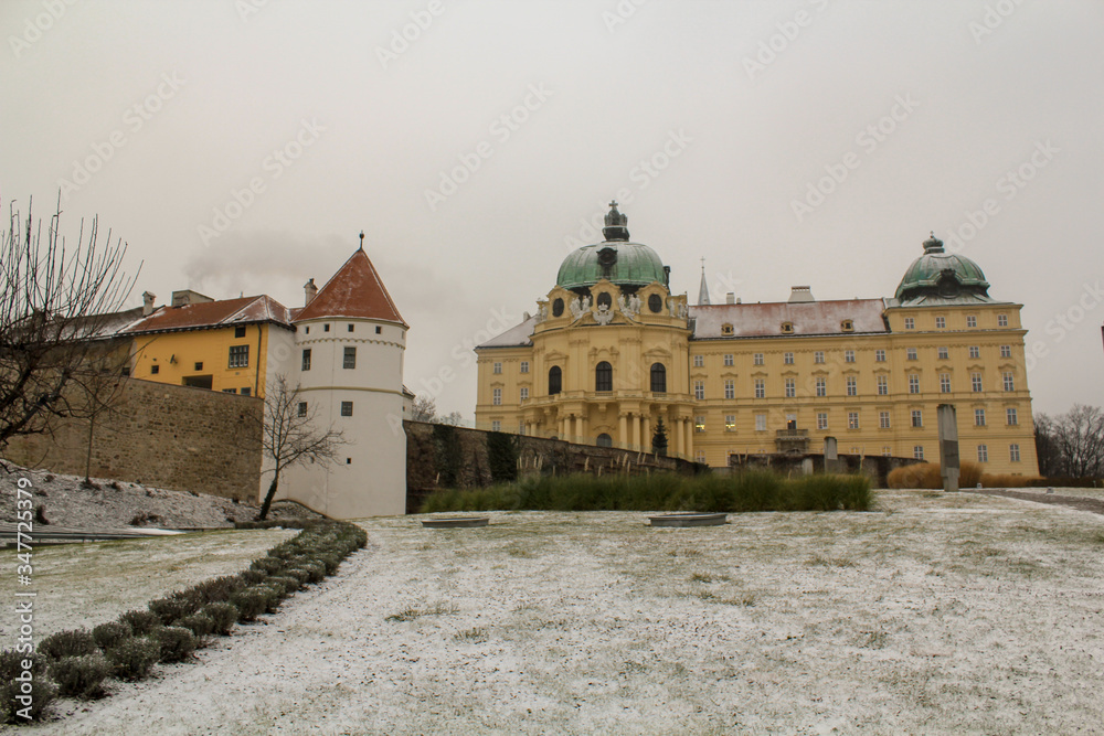 A green lawn covered with a thin layer of snow in front of an ancient Palace behind stone walls with free standing towers