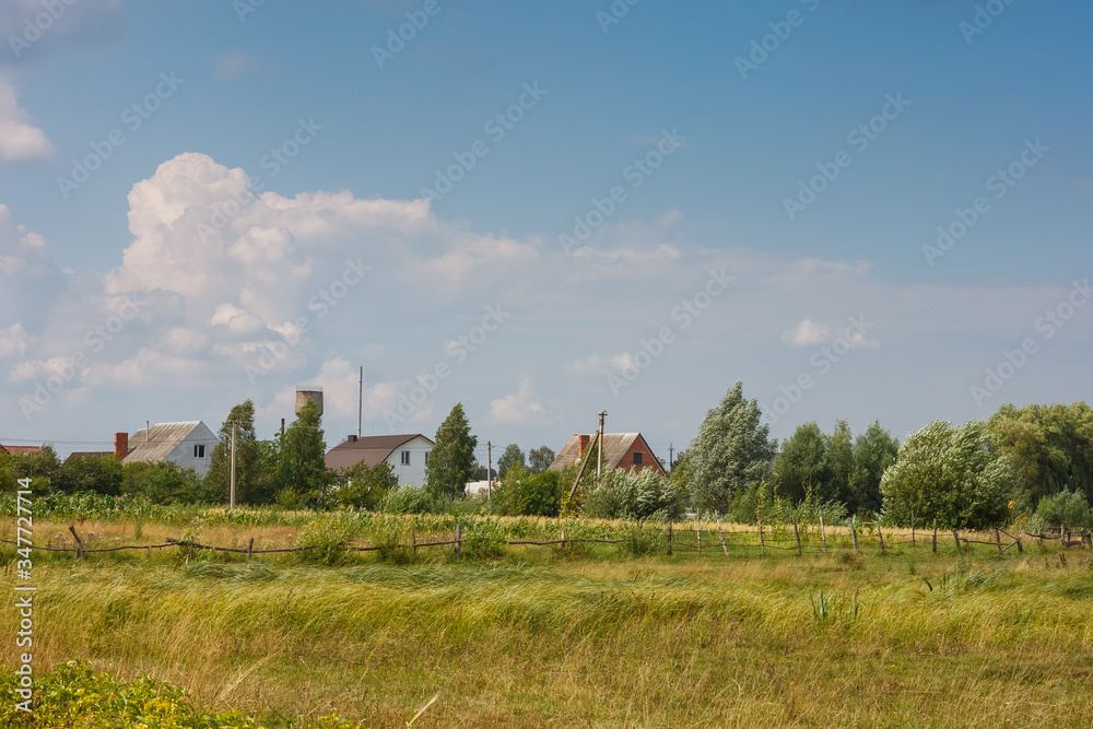 View of meadow with field, houses on the horizon and beautiful sky with clouds. Summer landscape.