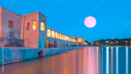 Fototapeta Naklejka Na Ścianę i Meble -  People resting in the ancient Khaju Bridge at twilight blue hour with full moon - Isfahan, Iran 