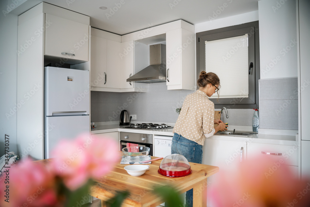 Young woman cooks food in her kitchen at home, washes food and dishes in the sink