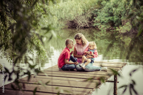 Mom with son and daughter. family of mother, daughter and son is sitting on a wooden bridge near the river. Family picnic. mother with children. Happy family on a walk